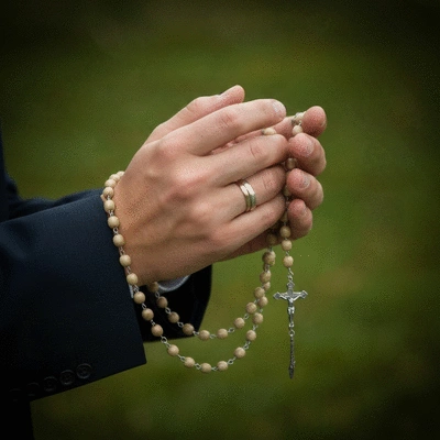 Ręce trzymające różaniec i modlące się, symbolizujące modlitwę za zmarłych